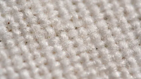 Nahaufnahme eines weißen Strickstoffs mit gleichmäßiger Noppenstruktur und feinen, abstehenden Fasern.
