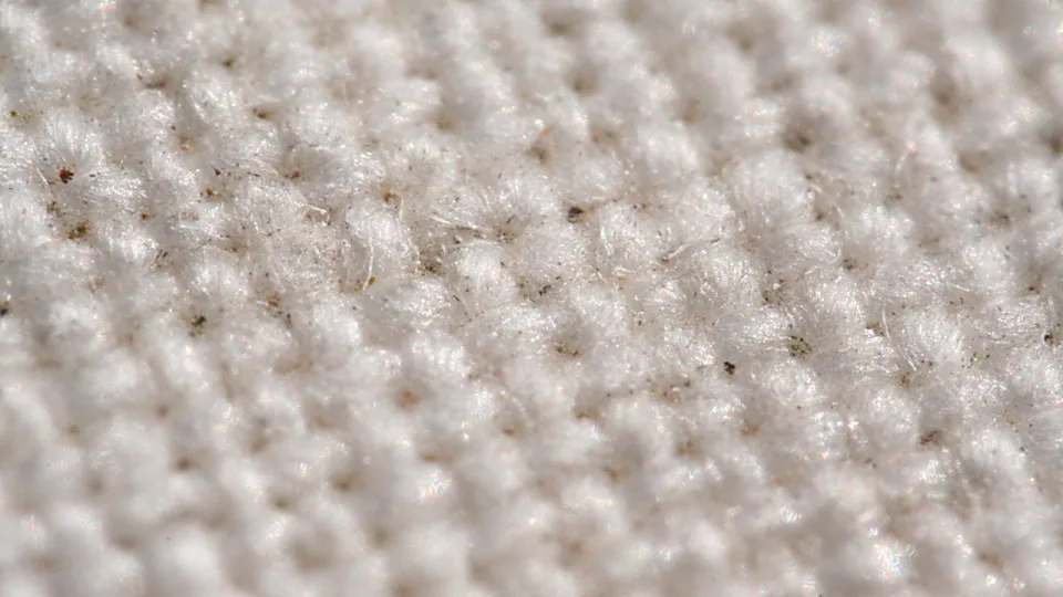 Nahaufnahme eines weißen Strickstoffs mit gleichmäßiger Noppenstruktur und feinen, abstehenden Fasern.