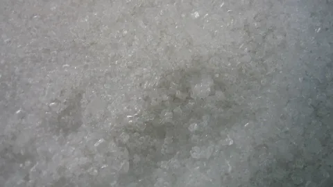 Nahaufnahme von dicht gepackten, weißen Kristallkörnern mit glitzernden Kanten und Lichtreflexen.