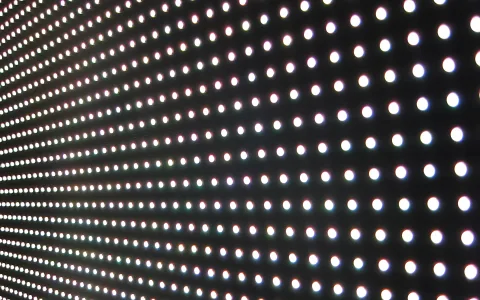 Nahaufnahme einer LED-Anzeige mit vielen weißen und farbigen Leuchtpunkten in einem regelmäßigen Raster auf schwarzem Grund, leicht perspektivisch schräg aufgenommen.