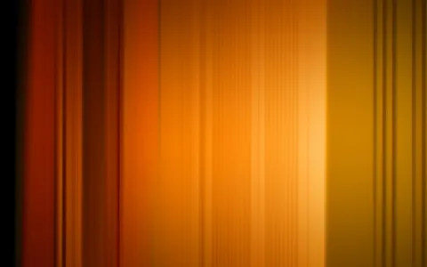 Unscharfe vertikale Streifen in Orange, Rot und Gelb, die von dunklem Rand links zu hellem Lichtbereich rechts verlaufen.