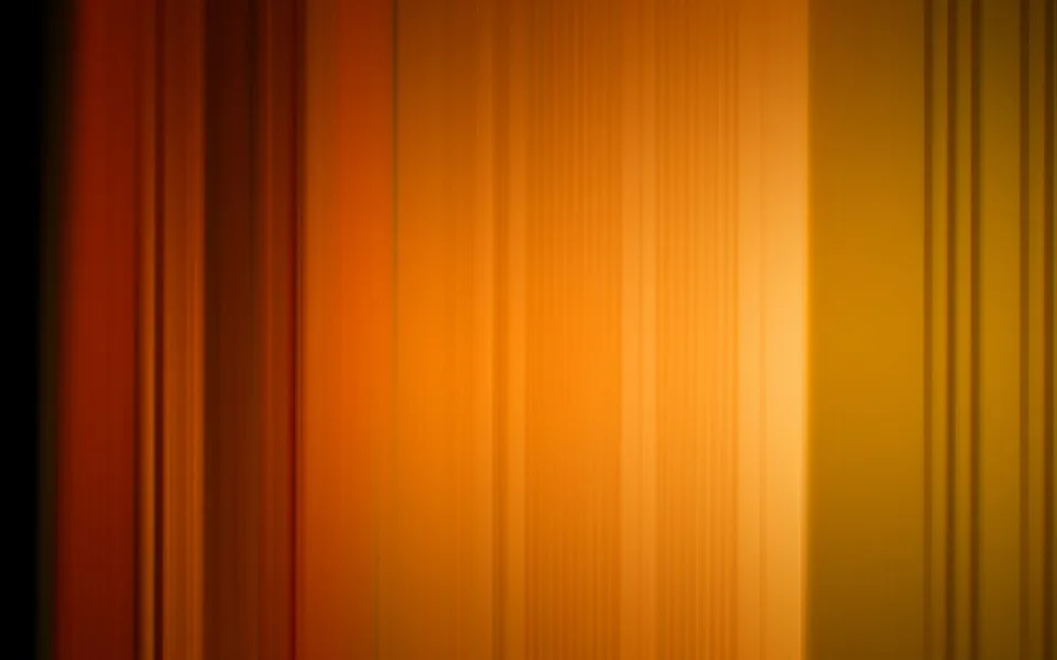 Unscharfe vertikale Streifen in Orange, Rot und Gelb, die von dunklem Rand links zu hellem Lichtbereich rechts verlaufen.