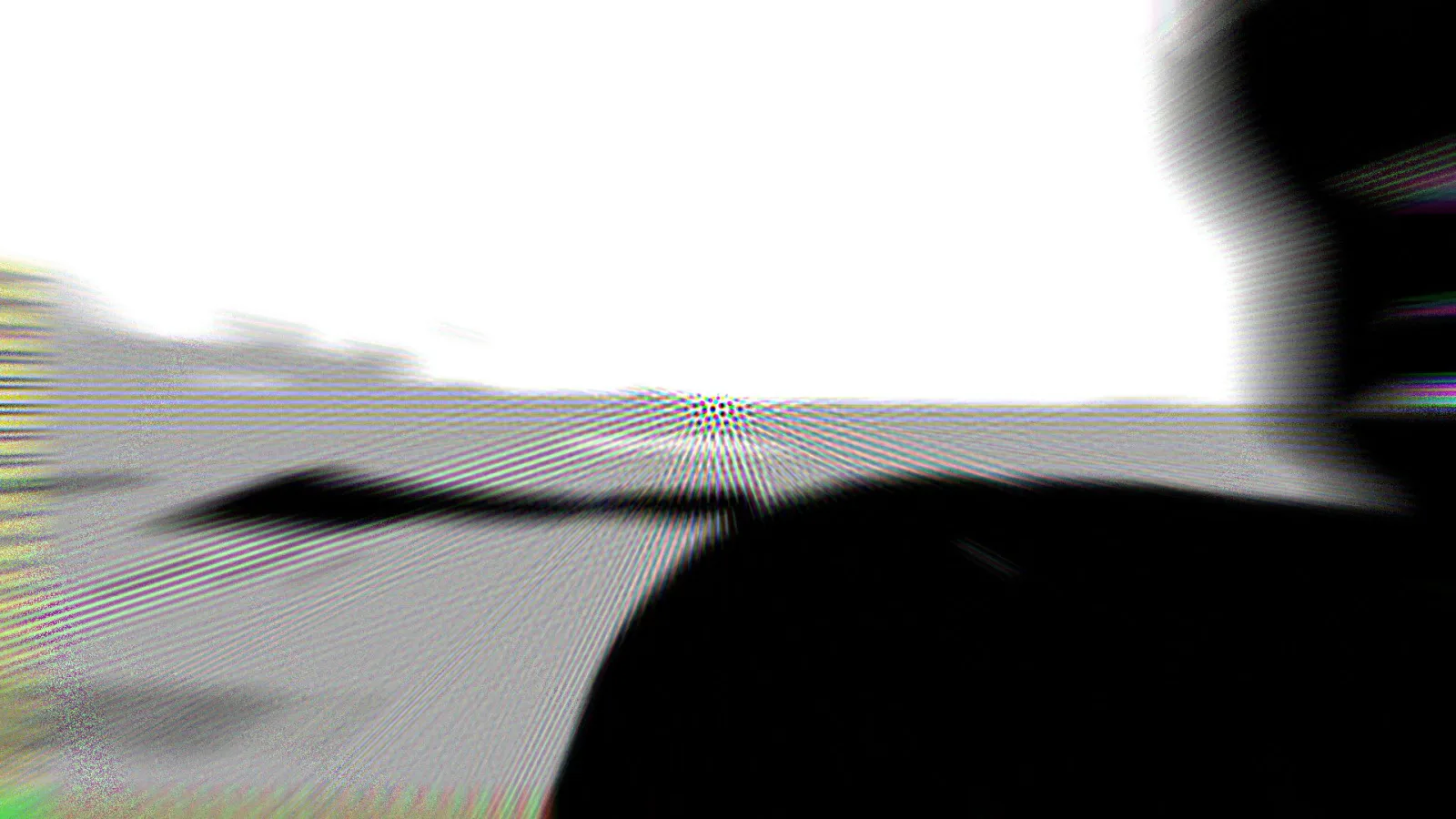 Abstrakte Schwarzweiß-Aufnahme mit weißem Himmel oben, grauer Fläche und einer großen schwarzen Form rechts unten, dazu Moiré-Muster und farbige Schlieren am Rand.