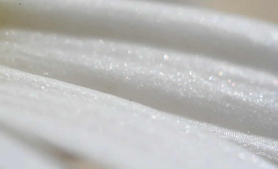 Nahaufnahme weißer Blütenblätter mit glitzernden Lichtpunkten auf sanft geschwungenen Flächen.