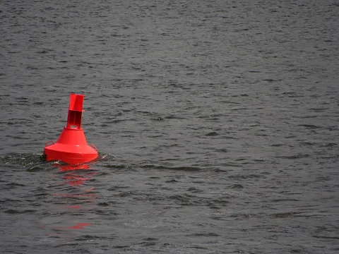 Eine rote Boje ragt links aus unruhigem, dunkelgrauem Wasser.