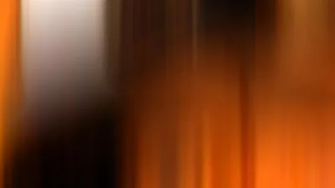 Vertikal verwischte Streifen in Orange, Braun und Schwarz, oben links ein heller Bereich.