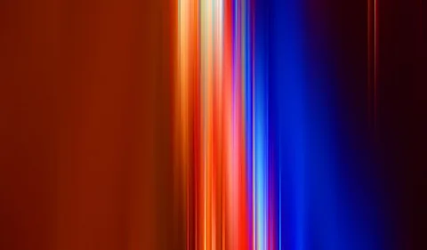 Vertikale, verwischte Lichtstreifen in Orange, Rot, Weiß und Blau auf dunklem Hintergrund, links ruhige orangefarbene Fläche.