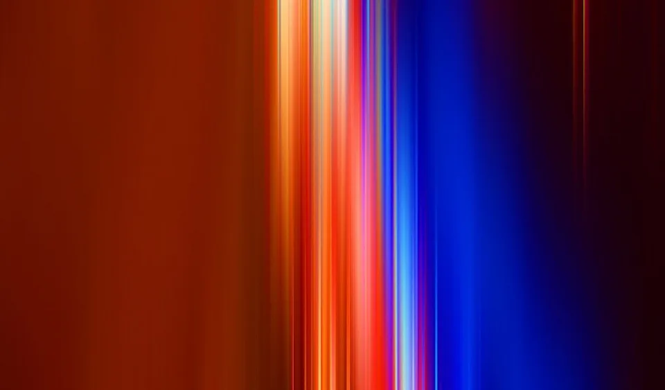 Vertikale, verwischte Lichtstreifen in Orange, Rot, Weiß und Blau auf dunklem Hintergrund, links ruhige orangefarbene Fläche.