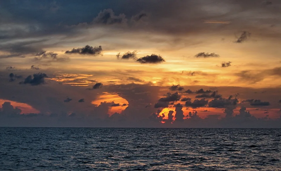 Sonnenuntergang über dem Meer, orange leuchtende Wolken vor dunklem Himmel über dem Horizont