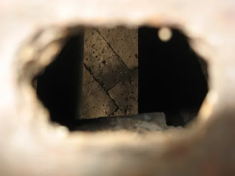 Blick durch ein unscharfes Loch in einer hellen Wand auf eine rissige Steinmauer im Schatten