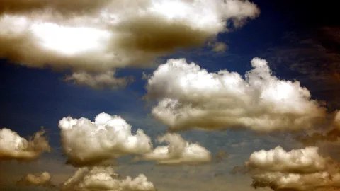 Weiße Kumuluswolken verteilen sich über einem tiefblauen Himmel, die Lichter liegen auf den Wolkenkuppen, der Rand wirkt leicht gedämpft und bräunlich.