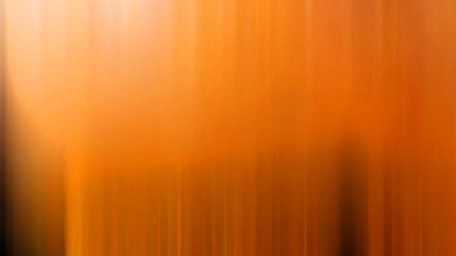 Vertikal verwischte Streifen in Orange- und Gelbtönen, oben heller, unten von dunklen Schatten durchzogen.