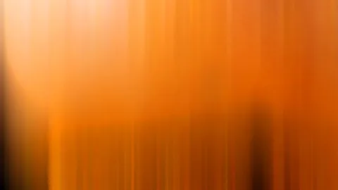 Vertikal verwischte Streifen in Orange- und Gelbtönen, oben heller, unten von dunklen Schatten durchzogen.