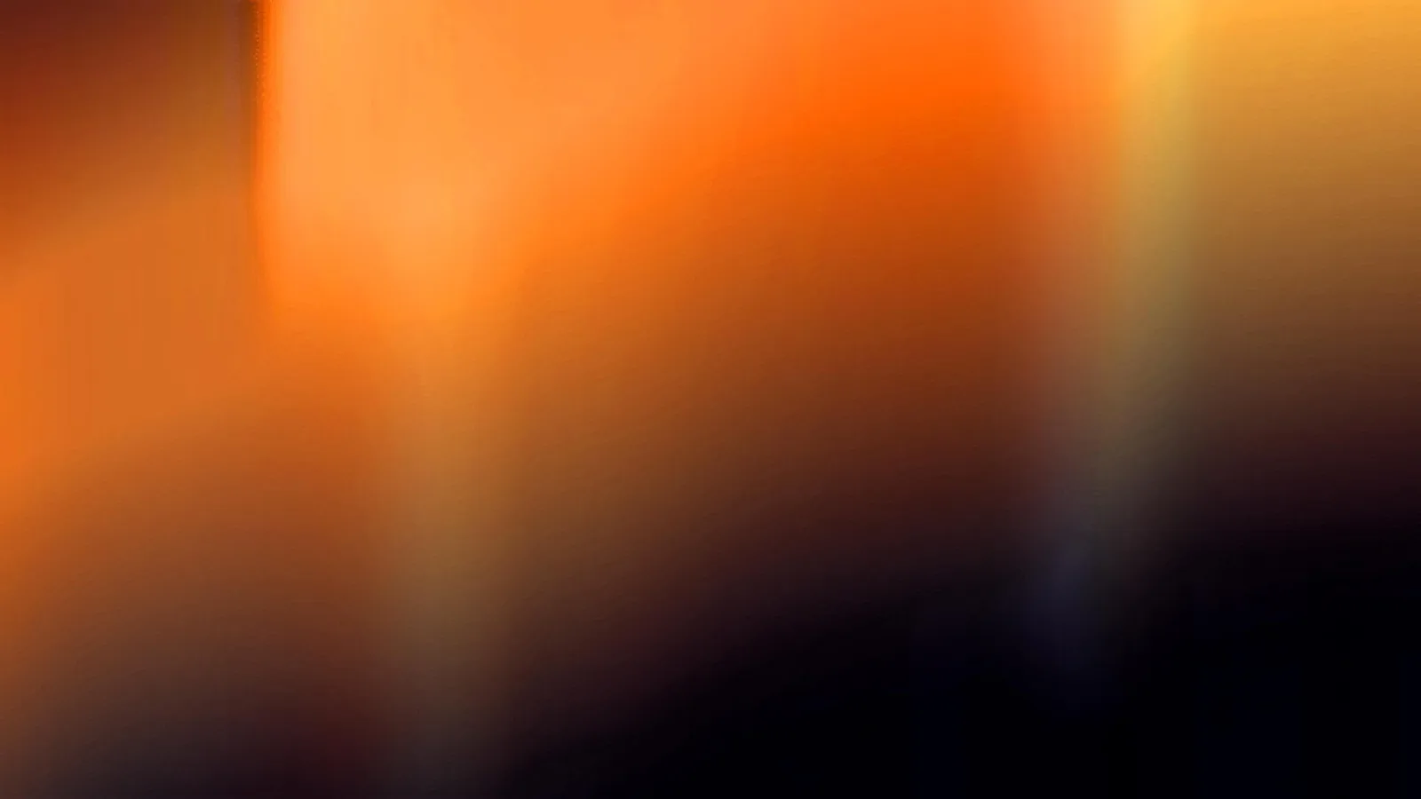 Unscharfer Verlauf von Orange nach Schwarz mit hellen vertikalen Lichtstreifen.