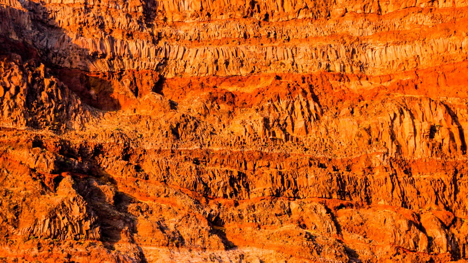 Steile, orangerote Felswand mit horizontalen Gesteinsschichten und scharfen Kanten im warmen Abendlicht.