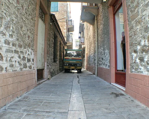 Schmale Gasse mit Steinmauern und rötlichen Sockeln, am Ende steht ein kleiner grün-gelber LKW zwischen den Hauswänden.
