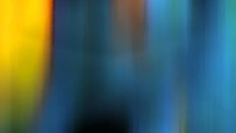 Abstrakte Aufnahme mit senkrechten Bewegungsschlieren: links leuchtendes Gelb, in der Mitte und rechts Blau- und Grüntöne, unten ein dunkler Bereich.
