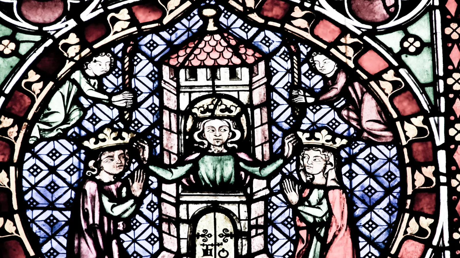 Buntes mittelalterliches Glasfenster mit einem gekrönten Herrscher in der Mitte, der von zwei gekrönten Figuren flankiert wird, darüber zwei kleinere Figuren, dahinter blau-weiß karierter Hintergrund.