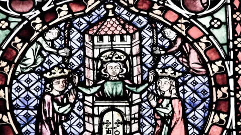 Buntes mittelalterliches Glasfenster mit einem gekrönten Herrscher in der Mitte, der von zwei gekrönten Figuren flankiert wird, darüber zwei kleinere Figuren, dahinter blau-weiß karierter Hintergrund.