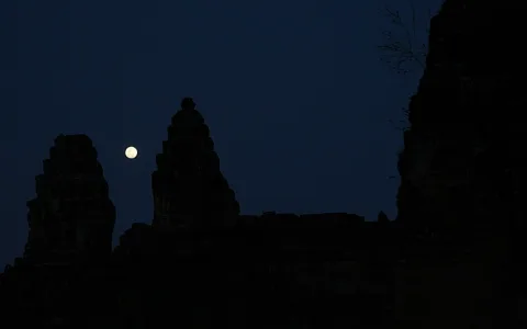 Dunkle Silhouetten mehrerer Tempeltürme vor einem nachtblauen Himmel, links neben den Türmen steht der helle Vollmond.