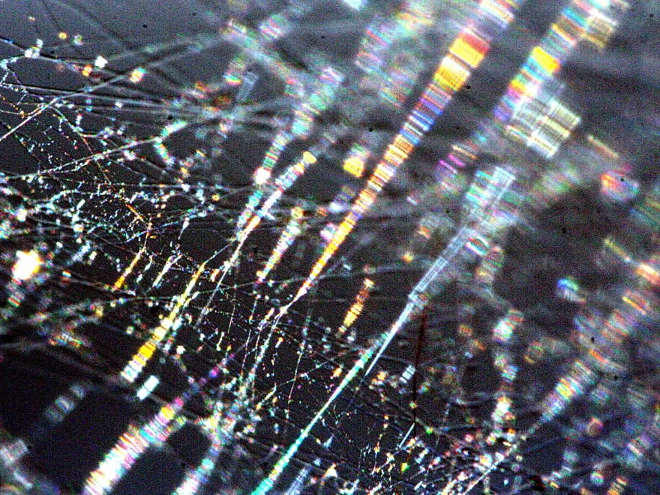 Dunkler Hintergrund mit leuchtenden, regenbogenfarbenen Lichtstreifen und feinen, glänzenden Spinnweben-Fäden.