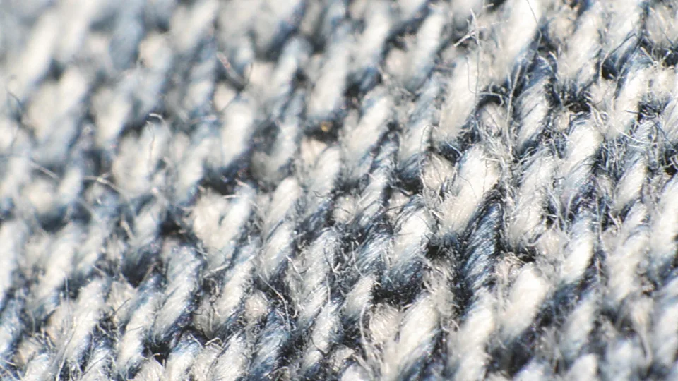Nahaufnahme eines grau-blauen Stoffs mit diagonalem Gewebemuster und feinen losen Fasern.