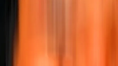 Abstrakte, senkrecht verwischte Farbflächen in Orange, links begrenzt durch einen dunklen Streifen.