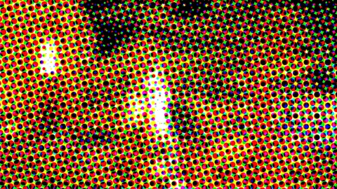 Dichtes Raster aus runden Punkten in Rot, Grün, Gelb, Blau und Schwarz, mit einem hellen weißen Lichtfleck in der Bildmitte.