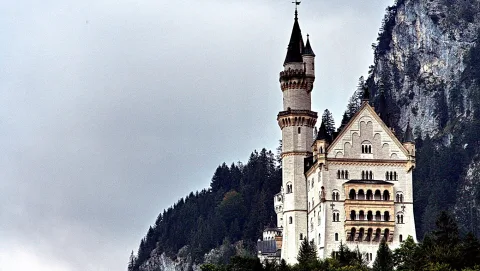 Schloss Neuschwanstein mit hohen Türmen auf einem bewaldeten Felsen unter grauem Himmel.