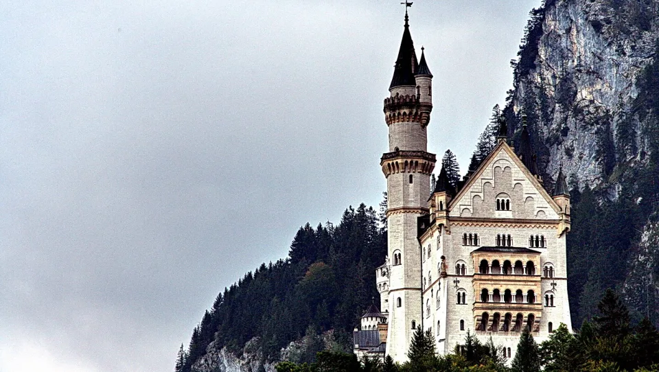 Schloss Neuschwanstein mit hohen Türmen auf einem bewaldeten Felsen unter grauem Himmel.