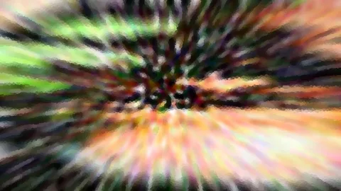 Abstrakte Aufnahme mit radialer Bewegungsunschärfe in Grün, Orange und Rosa, die von einem dunklen Zentrum nach außen strahlt, mit mosaikartiger Pixelstruktur.