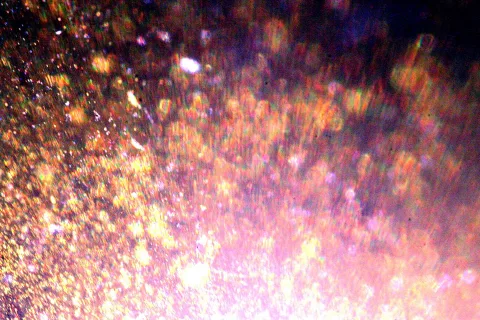 Nahaufnahme von glitzernden goldenen und rosafarbenen Partikeln vor dunklem Hintergrund, nach unten heller werdend