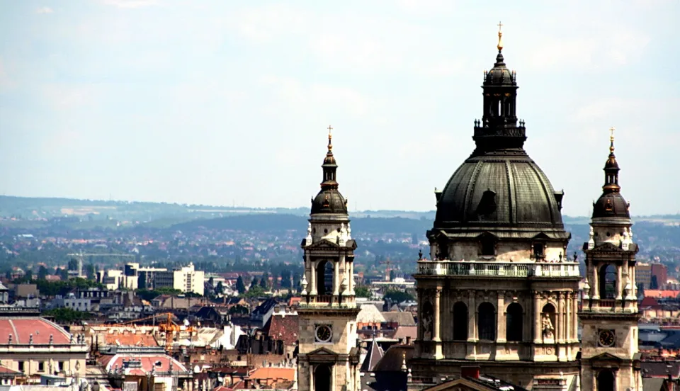 Kuppel und zwei Türme der Basilika vor einer weiten Stadtlandschaft mit Dächern und hellem, dunstigem Himmel