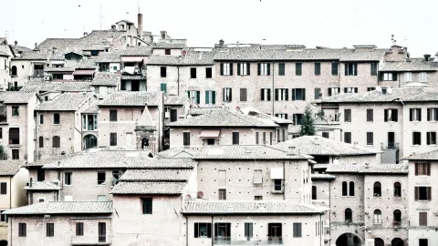 Dicht gedrängte Backsteinhäuser mit Ziegeldächern und Fensterläden in der Altstadt von Siena unter hellem, bedecktem Himmel.