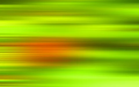Horizontal verwischte Streifen in Grün- und Gelbtönen, in der Bildmitte ein orangefarbener, unscharfer Lichtfleck.