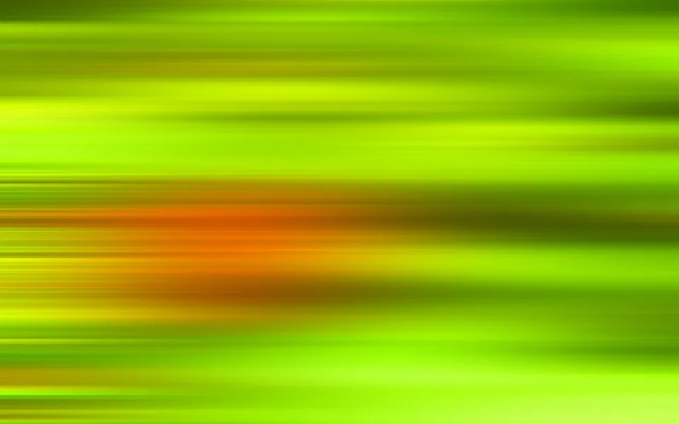 Horizontal verwischte Streifen in Grün- und Gelbtönen, in der Bildmitte ein orangefarbener, unscharfer Lichtfleck.