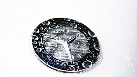 Silberner Mercedes-Stern auf einem schwarz-silbernen Emblem, darauf und daneben Wassertropfen auf weißem Untergrund