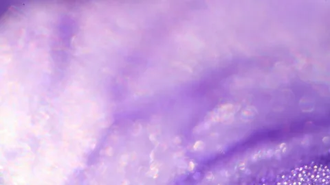 Unscharfe violette Makroaufnahme mit hellen Lichtreflexen und kleinen glitzernden Punkten in der rechten unteren Ecke