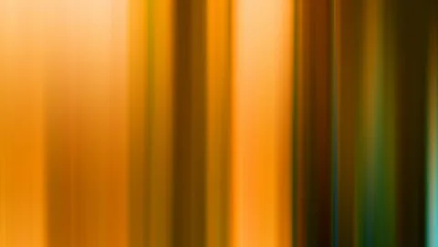 Unscharfe vertikale Streifen in Orange, Braun und Gelb, die von hell nach dunkel verlaufen, rechts am Rand ein schmaler grünlich-blauer Streifen.
