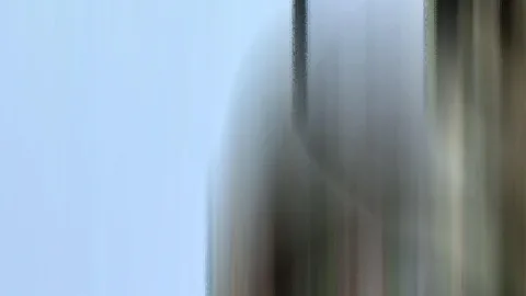 Stark verwischte, vertikale Streifen in Grau, Braun und Grün vor einem hellblauen Himmel auf der linken Seite.