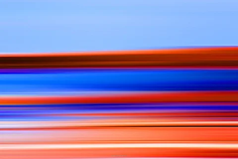 Horizontal verwischte Streifen in Blau, Orange, Rot und Violett, darüber ein hellblauer Himmel.