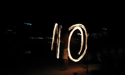 Ein Feuerwerfer in der Nacht zieht brennende Lichtspuren, die in den Himmel über einem dunklen Strand geschrieben scheinen.