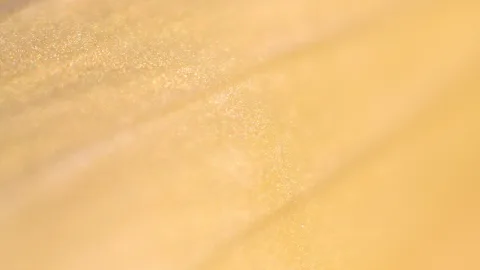 Nahaufnahme einer gelben Blütenblattoberfläche mit glitzernden Pollenkörnern und weich verlaufender Unschärfe
