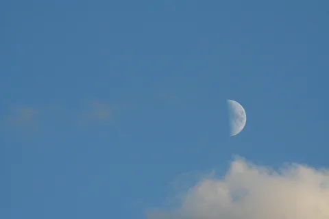Halbmond an einem klaren blauen Himmel, unten rechts eine helle Wolke