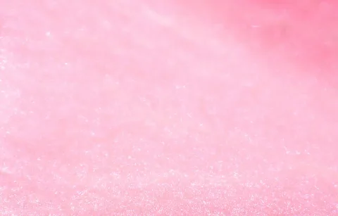 Nahaufnahme einer rosafarbenen, leicht unscharfen Oberfläche mit feinen hellen Glanzpunkten und einem Farbverlauf von Hellrosa zu kräftigerem Pink oben rechts.