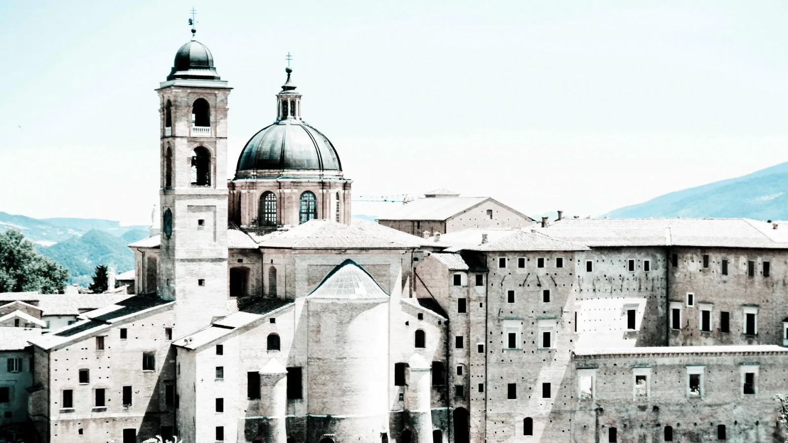 Historische Stadtansicht mit Kuppel und Glockenturm einer Kirche sowie mehrstöckigen Backsteingebäuden unter hellem Himmel