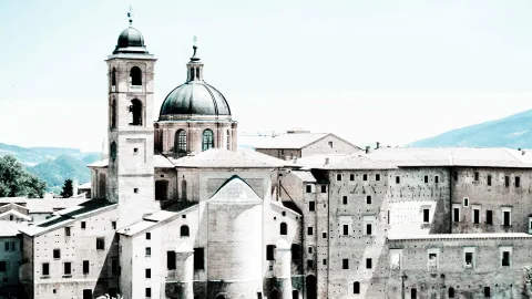 Historische Stadtansicht mit Kuppel und Glockenturm einer Kirche sowie mehrstöckigen Backsteingebäuden unter hellem Himmel