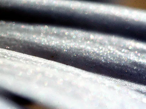 Nahaufnahme einer silbrig grauen, glänzenden Oberfläche mit diagonalen Streifen und vielen funkelnden Lichtpunkten.