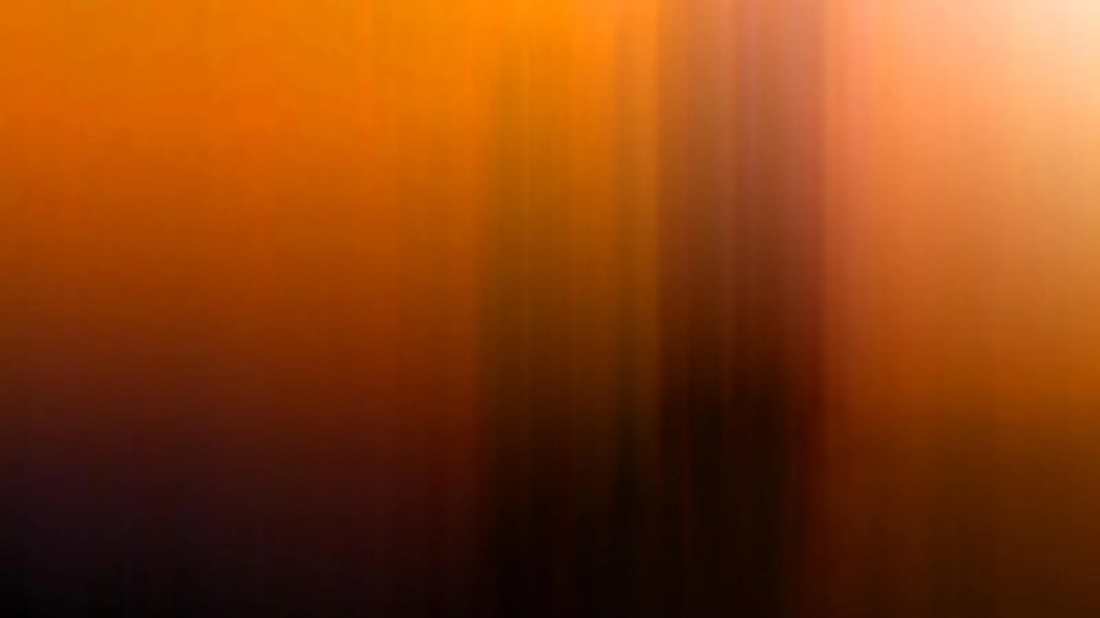 Abstrakte, verwischte vertikale Streifen in Orange, Braun und Dunkelviolett, oben rechts ein heller Lichtschein.