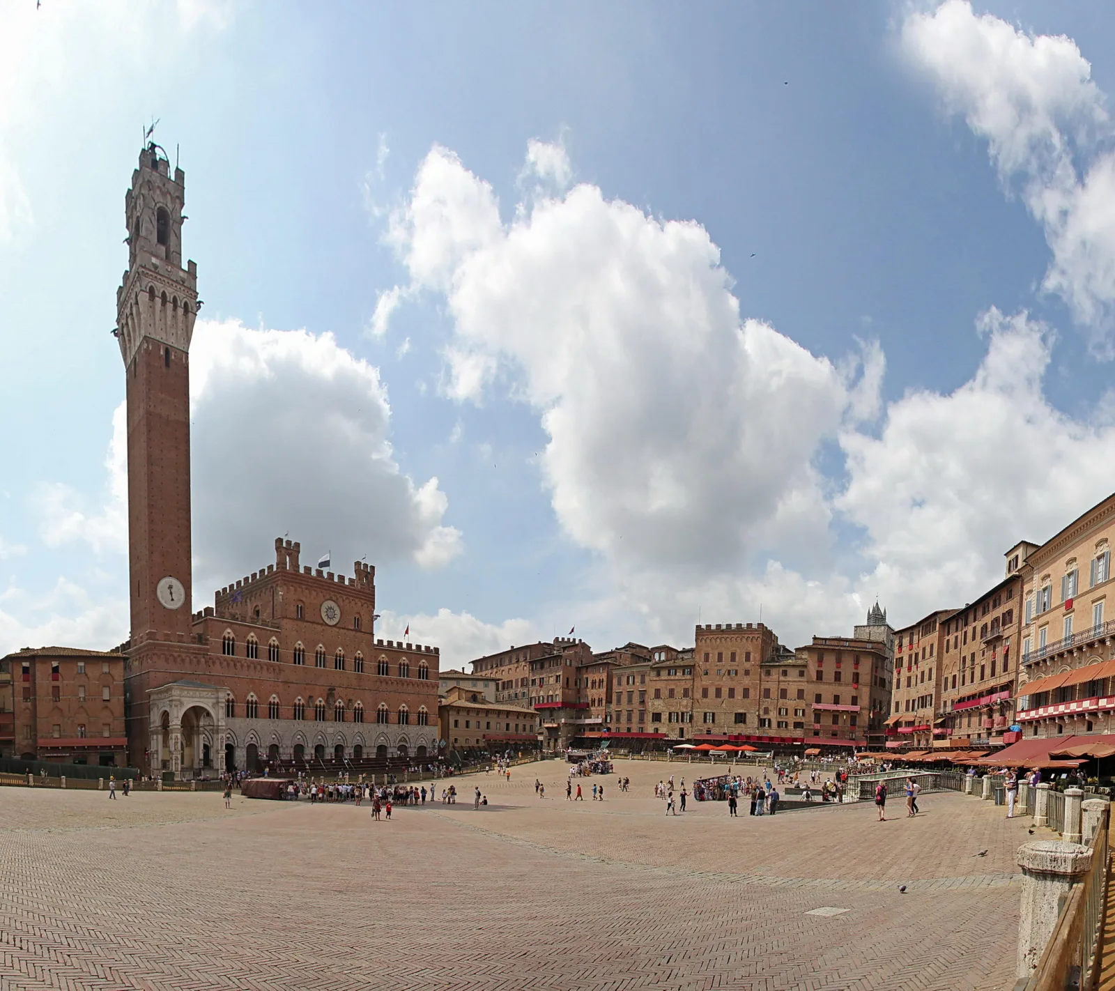 Weiter Platz mit Backsteinpalast und hohem Glockenturm in Siena, davor Menschen und Cafés unter blauem Himmel mit Wolken.